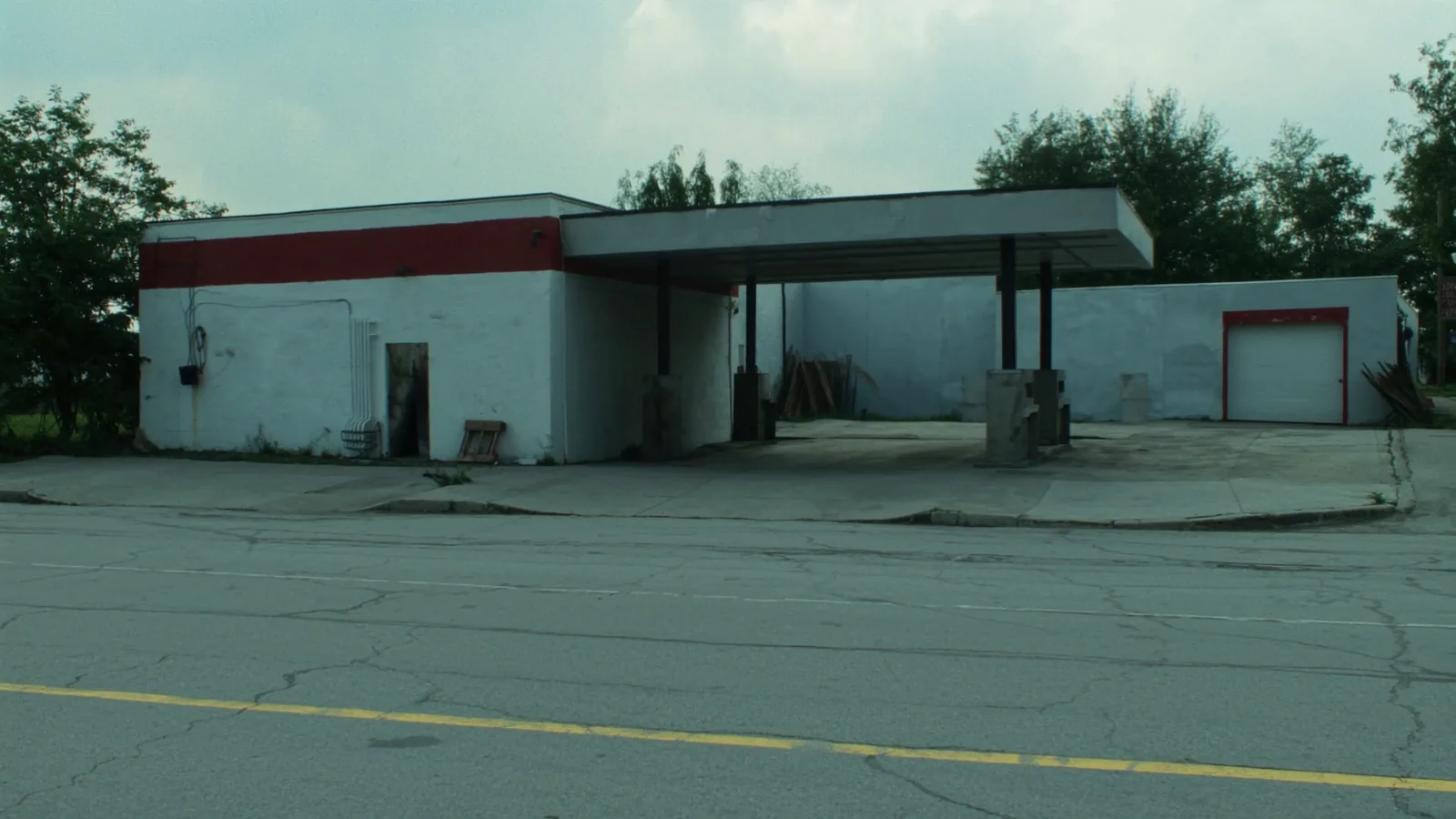An abandoned mid century filling station on a small town corner, its canopy still standing over bare concrete where the pump islands were removed.